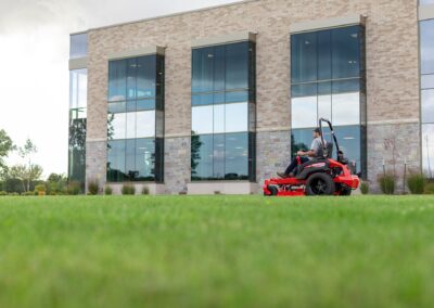 Person riding a red lawnmower on a grassy area in front of a modern building